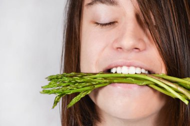 A man holds a bunch of asparagus in his teeth. Man enjoying eating fresh asparagus. Healthy plant-based diet, vegetarianism, good eating habits, Natural nutritious food. healthy lifestyle clipart