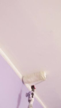  Uzatma çubuğu olan paten tavana beyaz boya sürüyor. İç mekan gelişimi. Resim servisi. Resim malzemeleri ve boya malzemeleri satışı. resim süreci