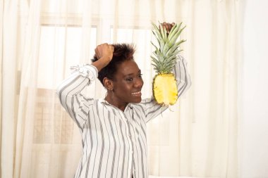 Kısa, modern saç kesimi olan Afrikalı siyahi kadın sağlıklı bir yaşam tarzı sergiliyor. Elinde olgun bir ananas tutuyor. Sağlıklı alışkanlıklar, neşe, olumlu, meyvecilik