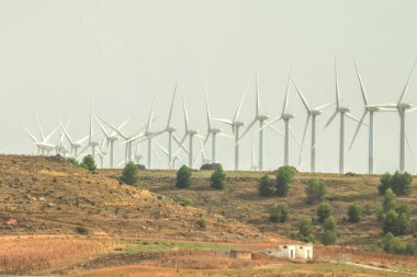 Rüzgâr türbinleri kırsal bir alanda bulutlu bir gökyüzünün altında. Rüzgâr çiftliğinde elektrik üretimi. Yeşil çevre dostu enerji. Enerji eksikliği. Elektrik kesintisi, elektrik kesintisi, rüzgar türbinlerinin durması, elektrik kesintileri.