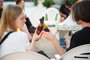 Dışarıdaki bir partide bira şişelerini tokuşturan iki genç insan. Alkol gençlerin elinde.