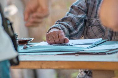 Yaşlı adamlar el şeklinde bir klasörün üzerinde duruyor. Masasında da belgeler var. Emekliler çalışıyor. Emeklilik masrafları. Yaşlı adam kayıtları, yatırım istatistiklerini, ev giderlerini tutuyor..