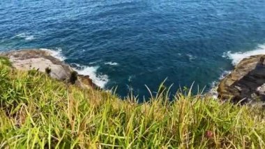 Cabo Frio, Rio de Janeiro - Brezilya. Yukarıdan panoramik manzara - Praia da Concha, sahil bitki örtüsü, dağlar, kayalara vuran dalgalar. Çarpıcı mavi deniz suyu. Jetski arka plandan geçiyor..