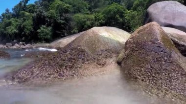 Dalgalar sahile yaklaşıyor. Su kayalara çarpıyor. Arka planda bitki örtüsü var. Ilha Grande Brezilya.