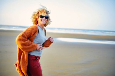 Genç, sarışın, beyaz bir kadın güneşli bir günde plajda koşuyor. Berria plajı, Cantabria, İspanya, Avrupa.