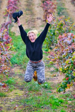 Üzüm bağı tarlasına atlayan neşeli, olgun, genç sarışın çiftçi kadın. Iguzkiza, Navarre, İspanya, Avrupa.