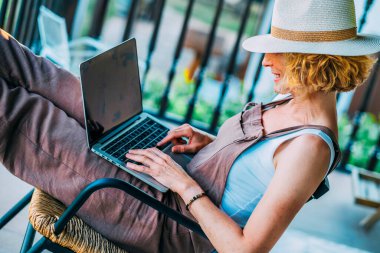 Önünde dizüstü bilgisayarı olan bir kadın sandalyede oturuyor. Zamanının tadını çıkarıyor.