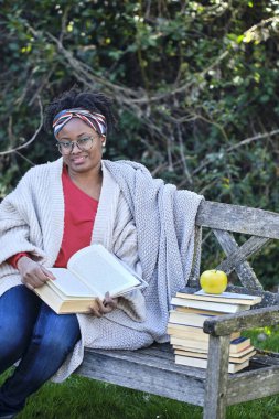 Bir kadın bir kitap yığını ve bir elmayla bankta oturuyor. Gözlük ve eşarp takıyor. Yaşam tarzı kavramı.
