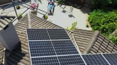 Güneş panelleri çatıya monte edilirken güneşli bir bahçede güneşlenen iki kadın görülüyor. 4 bin. Sahne çevre dostu ve rahatlatıcı ortamı vurguluyor.