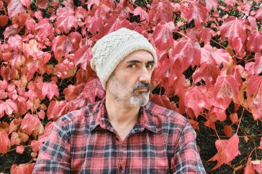 İşaretli gömlek ve güz yapraklı yün şapka giymiş olgun bir beyaz adamın portresi..