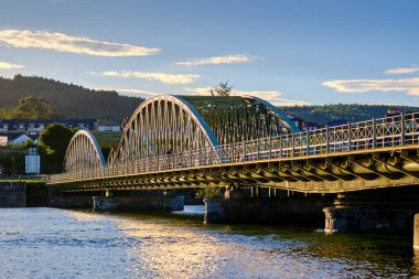 Elegant arch bridge crossing a serene river under a clear blue sky. Colindres, cantabria, spain clipart