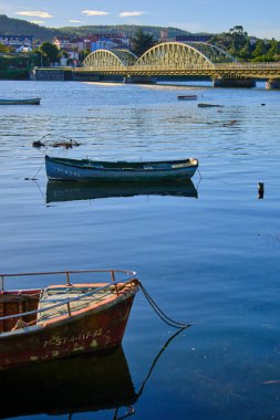 Small boats floating on a calm river near an arched bridge. Ason river. Colindres, cantabria, spain clipart