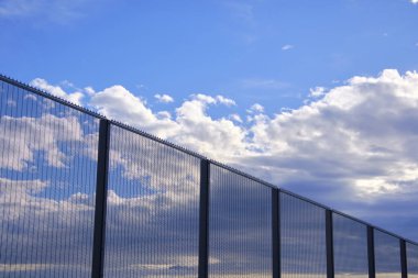 Şeffaf yüksek güvenlik çiti bulutları ve gökyüzünü yansıtıyor, güzel mavi gökyüzünün altında havaalanı çevresini koruyor.