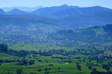 Yeşil vadi, ekili tarlalar ve arka planda dağlarla çevrili evler güneşli bir günde. Cantabria, İspanya.