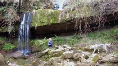 Sarışın yürüyüşçü köpeğiyle birlikte küçük bir şelalenin yanında dinleniyor. Şelale yolu. Esles, Santa Maria de Cayon, Cantabria, İspanya. Yüksek kalite 4k görüntü
