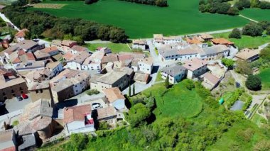 Yeşil çayırlar ve ağaçlar, İspanya 'nın sakin kırsallarına yerleşmiş kırmızı kiremitli çatıları olan küçük bir köyü kucaklıyor. Iguzkiza, Navarre, İspanya. İHA görüntüsü. Yüksek kalite 4k görüntü