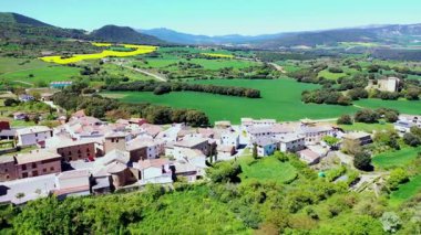 Büyüleyici köy, yemyeşil bitki örtüsü ve güneş ışığıyla yıkanmış yuvarlanan tepelerle çevrili. Iguzkiza, Navarre, İspanya. İHA görüntüsü. Yüksek kalite 4k görüntü