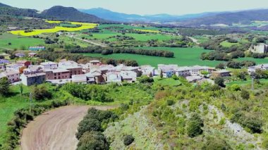 Etrafı yuvarlanan yeşil tepeler ve İspanya kırsalında canlı sarı tarlalarla çevrili sakin bir köy. Iguzkiza, Navarre, İspanya. İHA görüntüsü. Yüksek kalite 4k görüntü