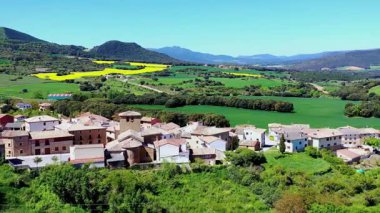 Etrafı yemyeşil tarlalarla çevrili sakin bir köy ve yuvarlanan tepeler güneşin altında güneşleniyor. Iguzkiza, Navarre, İspanya. İHA görüntüsü. Yüksek kalite 4k görüntü