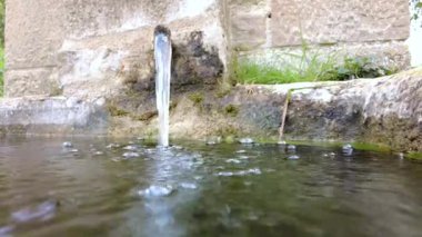 Metal bir borudan kristal berrak su akar ve taş bir havzada kabarcıklar ve kabarcıklar yaratır. Yüksek kalite 4k görüntü