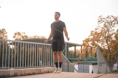 Siyah antreman kıyafetleri giyen çocuk ip atlıyor. Sonbahar sezonu boyunca sokaklarda antrenman yapıyor..