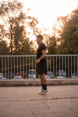 Siyah antreman kıyafetleri giyen çocuk ip atlıyor. Sonbahar sezonu boyunca sokaklarda antrenman yapıyor..