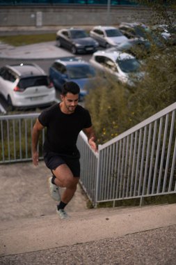 Siyah antreman kıyafetleri giymiş kaslı bacaklı çocuk aşağı yukarı eğitim görüyor. Sonbahar sezonu boyunca sokaklarda çitlerin yanında antrenman yapıyor..