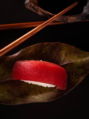 Ton balığı nigiri ve Japon suşi pilavı, siyah arkaplanlı lezzetli Japon yemeği ve doğu ve Asya yemek restoranları için yapraklarla ve soya sosuyla süslenmiş..