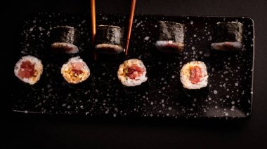 Zenital shot Tuna maki, Japon suşisi, siyah arkaplanlı lezzetli Japon yemeği ve yemek çubuklarıyla süslenmiş bir kase soya sosu, doğu ve Asya restoranları için..
