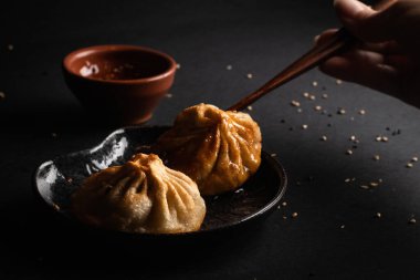 Lokanta, soya sosuyla birlikte bir Bao Zhi almak için çubuk kullanıyor. Doğu ve Asya yemek restoranları için siyah arkaplanlı lezzetli Japon yemekleri. Edamame salatası Japon yemeği, siyah arka planlı lezzetli Japon yemeği ve dekora sahip.