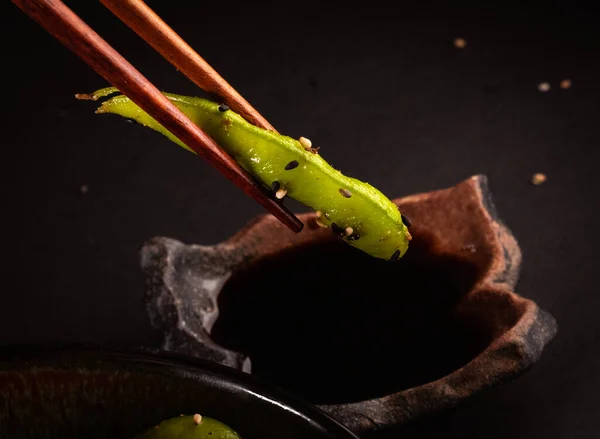 Edamame salad picked with Japanese chopsticks steamed, delicious Japanese food with black background and decorated with leaves and a wicker basket, for oriental and Asian food restaurant.