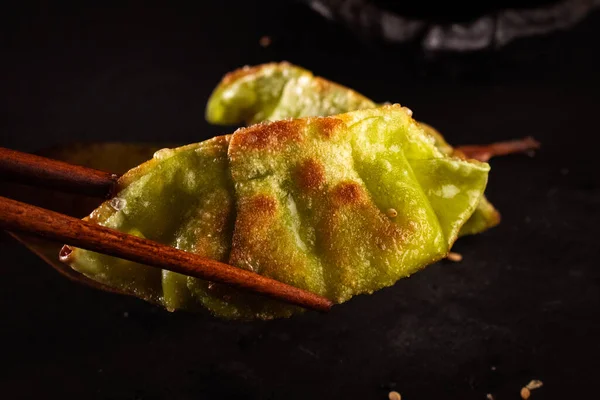 Japanese steamed green vegetable gyozas, delicious Japanese food with black background and decorated with leaves and a wicker basket, for oriental and Asian food restaurant.
