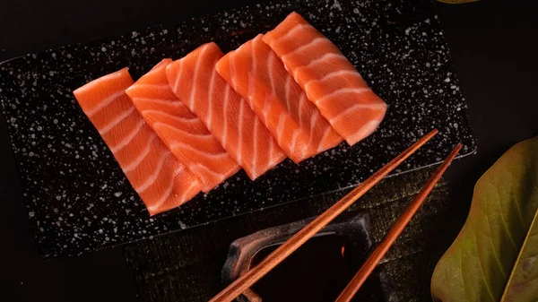 Japanese salmon sushi sashimi, delicious Japanese food with black background and decorated with leaves and soy sauce, for oriental and Asian food restaurant.