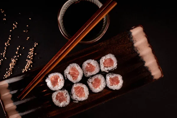 Tuna maki, Japanese sushi, delicious Japanese food with black background and decorated with chopsticks and a bowl of soy sauce, for oriental and Asian food restaurant.