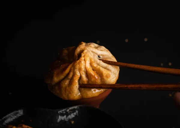 Close up about a diner uses chopsticks to pick up a Bao zhi accompanied by soy sauce delicious steamed Japanese food with black background for oriental and Asian food restaurant.Backgrounds and images for oriental and asian food restaurants.