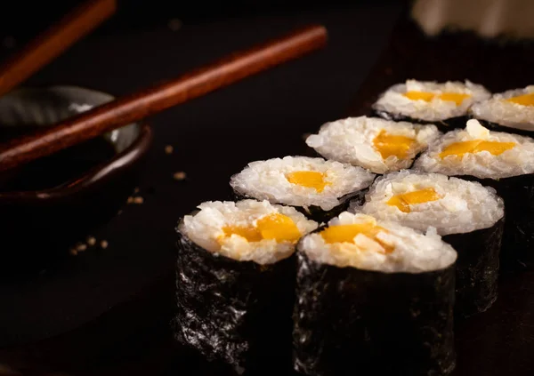 close up ,Cheese and mango maki, Japanese sushi, delicious Japanese food with black background and decorated with chopsticks and a bowl of soy sauce, for oriental and Asian food restaurant.