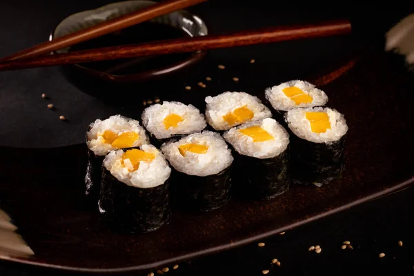 Cheese and mango maki, Japanese sushi, delicious Japanese food with black background and decorated with chopsticks and a bowl of soy sauce, for oriental and Asian food restaurant.