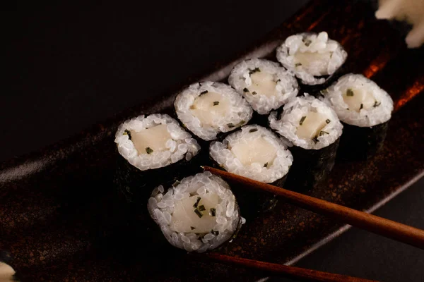 Butterfish maki, Japanese sushi, delicious Japanese food with black background and decorated with chopsticks and a bowl of soy sauce, for oriental and Asian food restaurant.