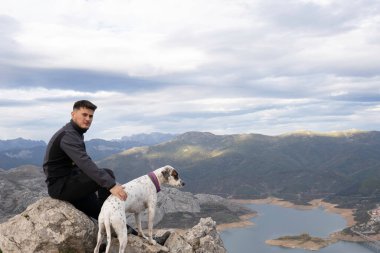 Dağın tepesinde koyu renk dağ kıyafetleri giymiş genç dağcı bir kayanın üzerinde dinleniyor. Arka planda bir göl ve komşu sıradağları görebiliyoruz. Yürüyüş ve tırmanış için duvar kağıtları.