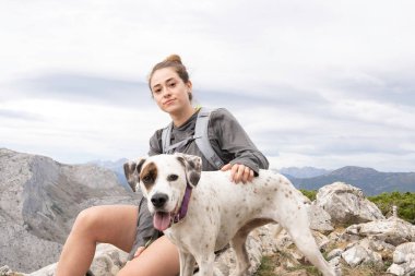 Dağ kıyafetleri ve gri bir sırt çantası giymiş genç beyaz bir kız. Bu macerada köpeği ona eşlik ediyor. Arka planda dağ sırasını görebilirsiniz. Yürüyüş ve tırmanış için duvar kağıtları.