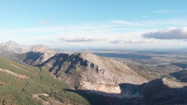 Ufukta bir dağın yakınında dönen bir dronun panoramik görüntüsü var. Ormanları, nehirleri ve uzak bir köyü görebiliyoruz..