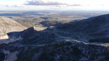 Arka planda büyük bir dağın gölgesinde uçan bir dronun hava görüntüsü küçük bir köyün yakınında bir orman ve nehir görüyoruz..