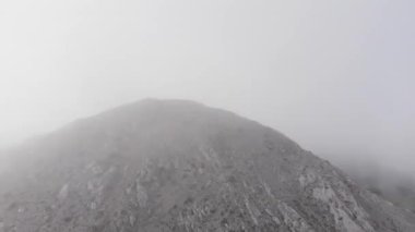 Kış sisi ile çevrili bir dağın zirvesini kaydeden bir dronun hava görüntüsü. Dağın hava aracı görüntüsü.