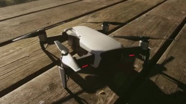  Saha masasının üstündeki beyaz bir dronun pervaneleri hareket ediyor. İnsansız uçak doğada ve ormanda uçmaya hazır..