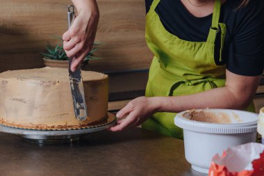 Tanınmayan bir kadın lezzetli katmanlı sünger keki çikolatalı kremayla süslüyor. DIY, dizi, adım adım, serinin bir parçası.