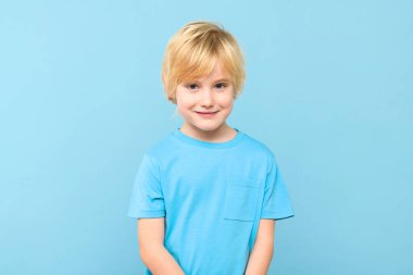 Günlük kıyafetli mutlu beyaz çocuk gülümsüyor, kameraya bakıyor, pastel mavi arka planda izole edilmiş..