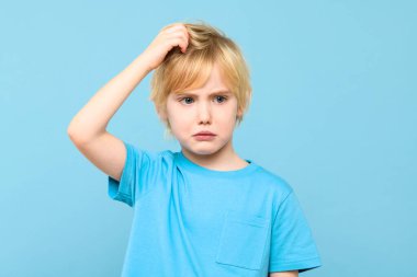 Kafası karışmış genç bir çocuk, kafa karıştırıyor, çözüm bulmaya çalışıyor, mavi arka planda izole edilmiş..