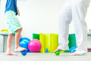 Seans sırasında çocuk ve kadın fizyoterapist. Fizyoterapide yalın ayak yüzey topuyla egzersiz yapan çocuk..