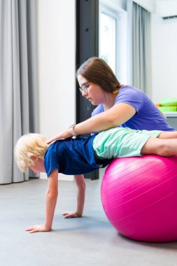 Kadın fizyoterapisti olan genç bir çocuk terapi seansı sırasında top kullanıyor. Çocuk fizyoterapisi. Çift taraflı koordinasyon.