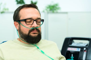 Oksijen terapisi, ayrıca ek oksijen olarak da bilinir. İnsan burun kanülünden oksijen soluyor. Konsantratör makinesine bağlı. Bağışıklık sistemini güçlendirir ve vücudun daha hızlı yenilenmesini destekler..